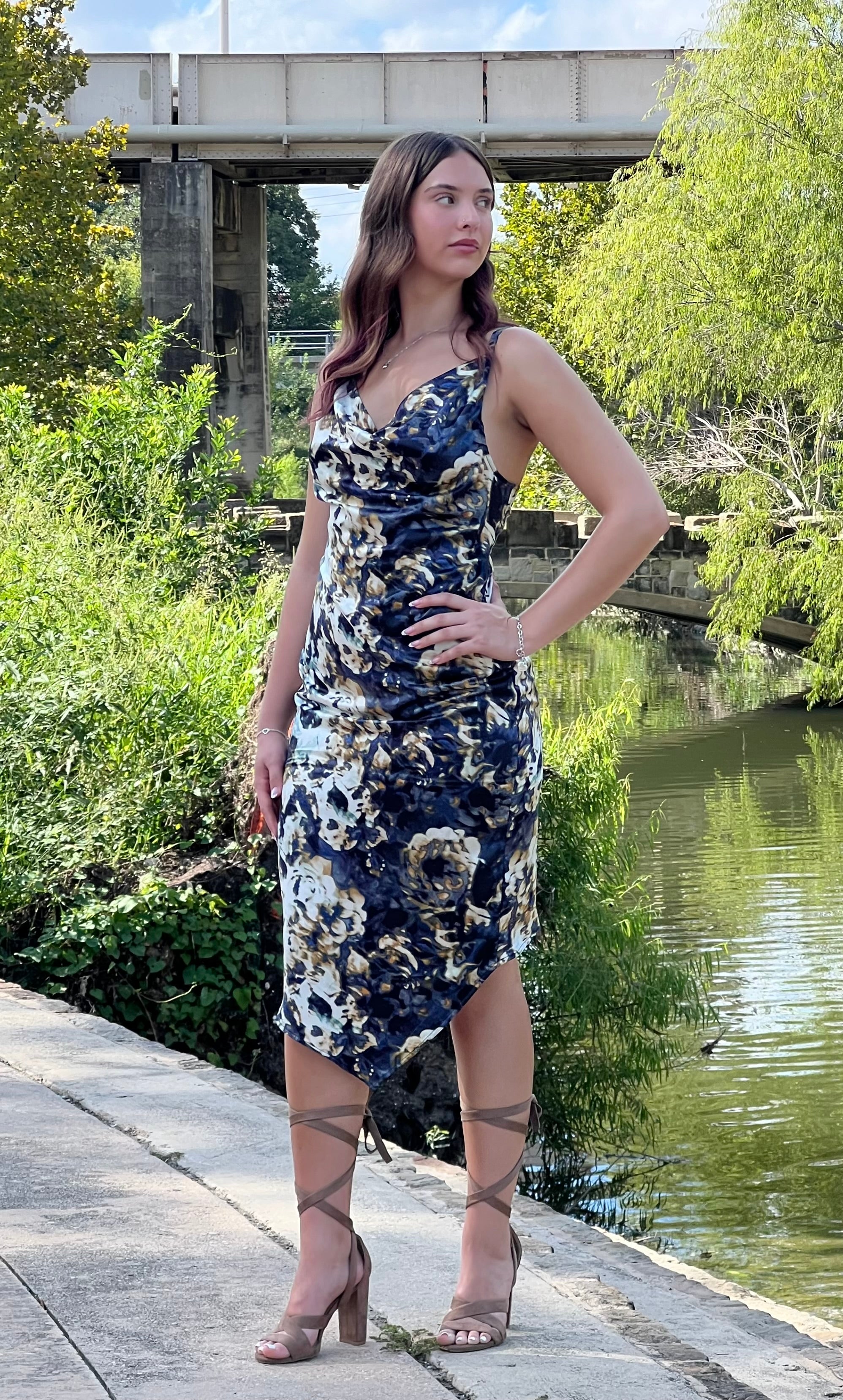 Woman in a floral dress standing by a river with greenery